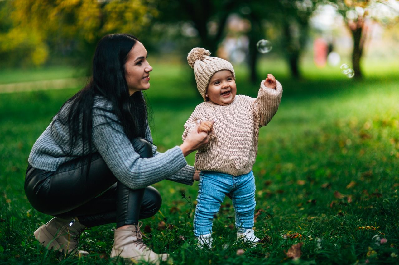 A joyful moment in the park with a mother and child playing with bubbles amidst green surroundings.