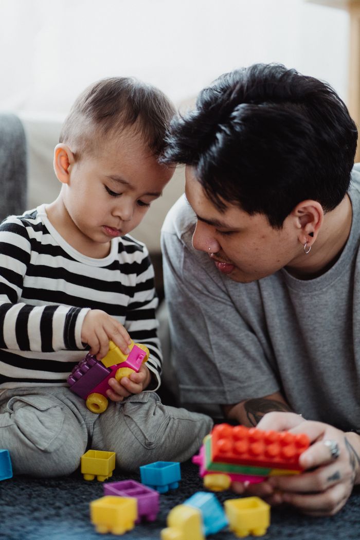 Father and toddler son bonding through play with colorful building blocks.